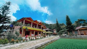 Una casa tradizionale con tetto rosso e tenda da sole gialla, immersa in un rigoglioso campo verde e un piccolo canale.