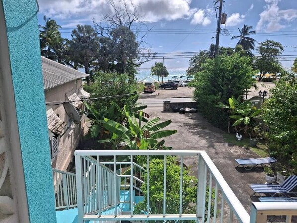 Zona residencial con una escalera que lleva a un balcón, un coche aparcado y una fila de sillas de descanso.