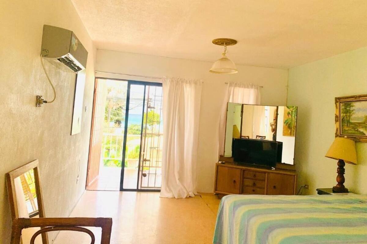 A room with a bed, a television on a wooden cabinet, a mirror, and a window with curtains.