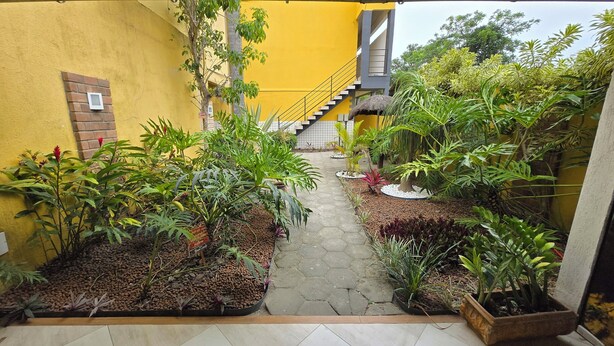 A narrow pathway flanked by potted plants and a yellow building with a staircase. - Residencial Valda, your accommodation in Cabo Frio. (Cabo Frio)