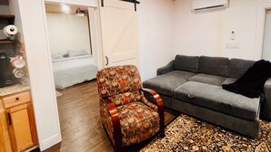 A living room with a sofa, patterned armchair, and a sliding door leading to a bedroom.