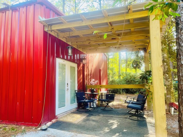 Un edificio rojo con un porche cubierto que tiene asientos al aire libre y una pérgola.