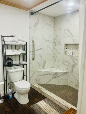 Un baño con inodoro, ducha con puerta de cristal, toallero y estante con artículos de aseo.