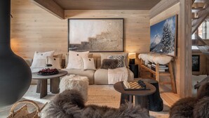 A cozy living room with a wooden ceiling, a large abstract painting, a sofa with fluffy cushions, a coffee table with a chess set, and a fireplace. - Chalet Quatre Coeurs with sauna in Saint Gervais (Saint-Gervais-les-Bains)