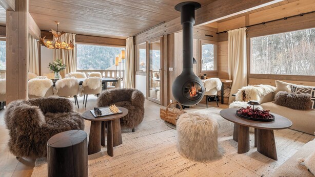 A cozy cabin interior with a central wood-burning stove, plush fur seating, and large windows offering views of a snowy landscape. - Chalet Quatre Coeurs with sauna in Saint Gervais (Saint-Gervais-les-Bains)