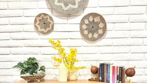 A wooden cabinet with multiple drawers, a vase with yellow flowers, and decorative plates on a white brick wall.