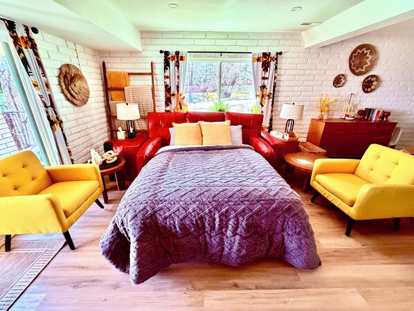 Un dormitorio moderno con una cama grande, dos sillones amarillos, un sofá rojo y un aparador de madera.