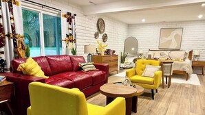 A modern living room with a red leather sofa, yellow armchairs, a wooden coffee table, and a bed with a white headboard.
