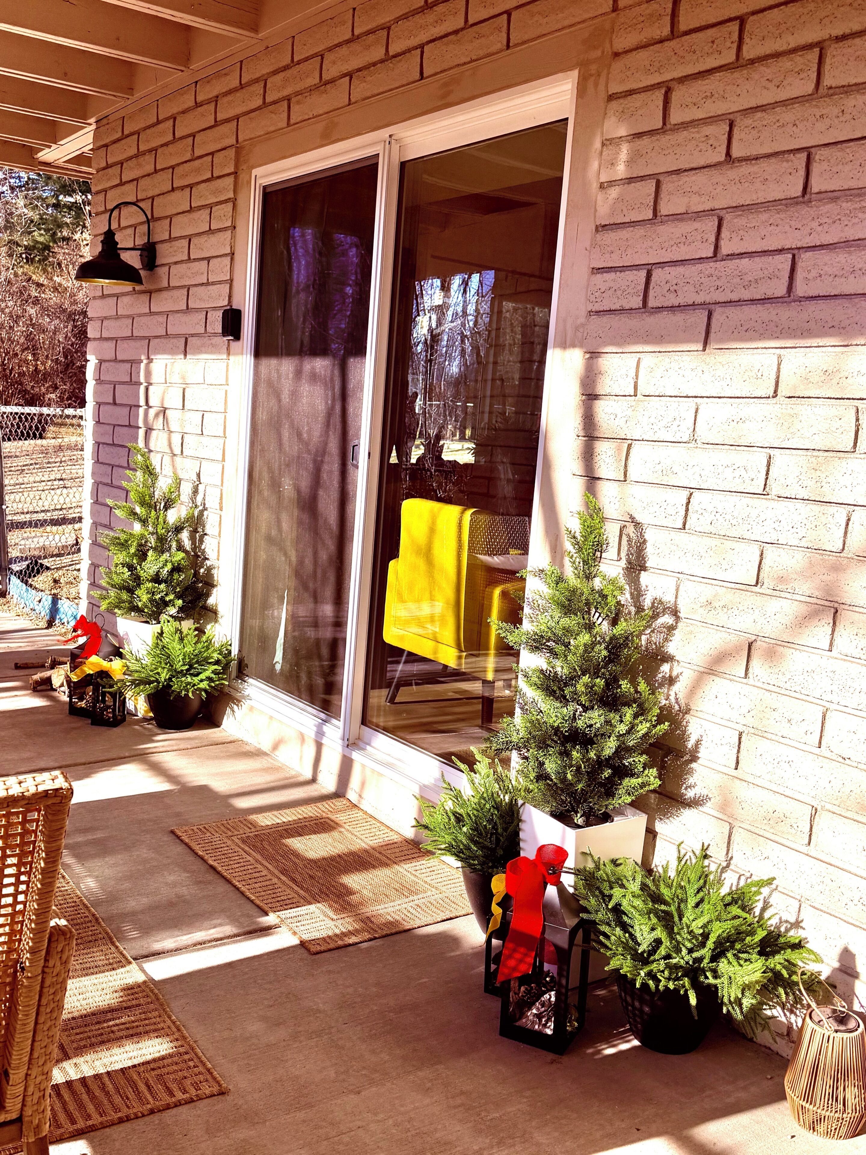 Un porche cubierto con puerta corrediza de vidrio, plantas en macetas y muebles de exterior.