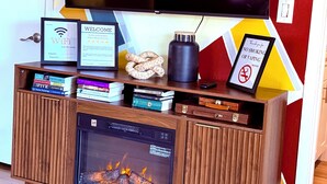 A wooden entertainment unit with a flat-screen TV, books, a framed welcome sign, a WiFi sign, a no-smoking sign, and a fireplace display.
