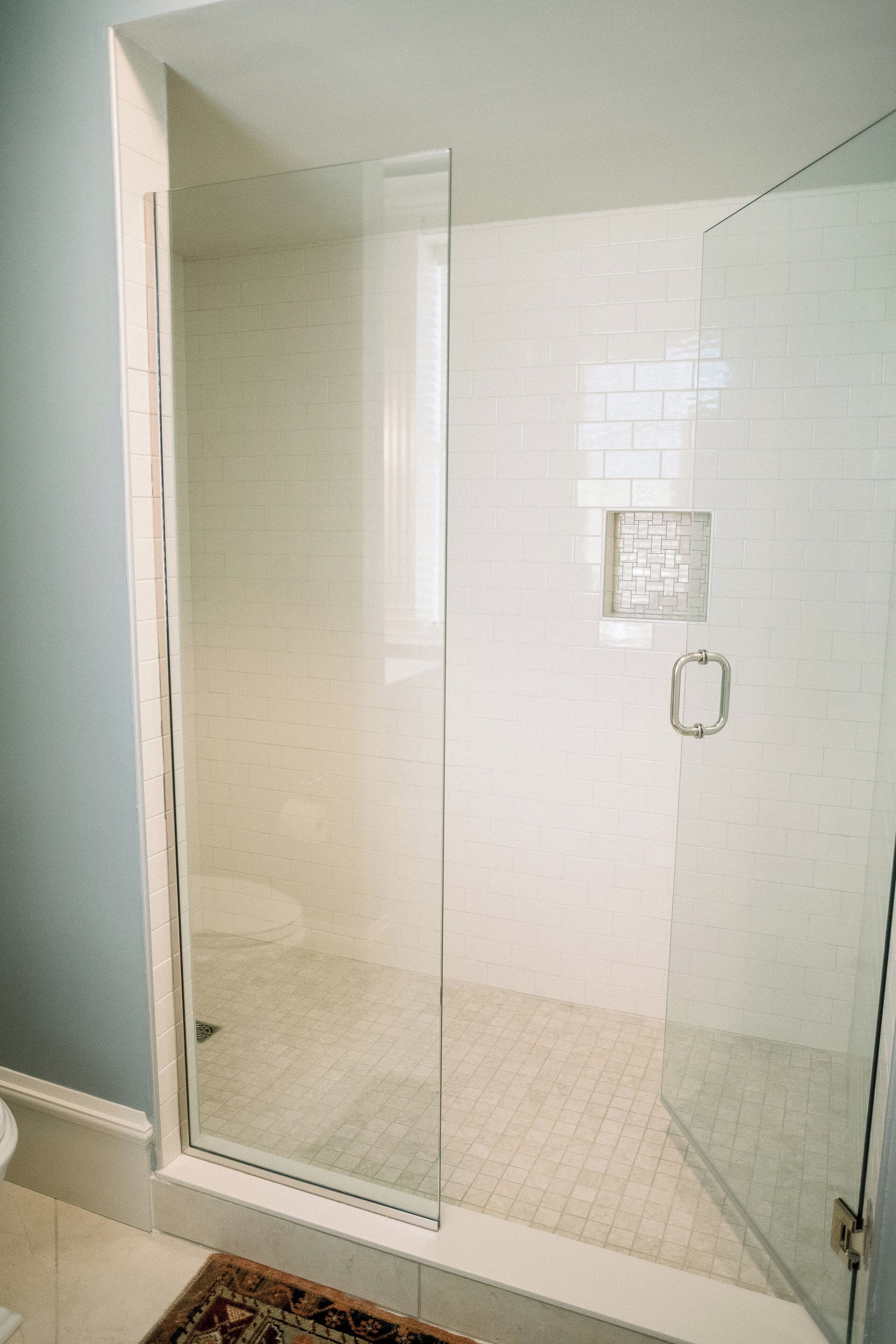 A glass-enclosed shower with white tiled walls and a small decorative tile pattern above the door.