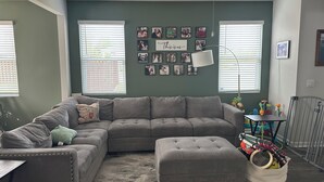 Een woonkamer met een modulaire bank, een voetenbankje en een wand met ingelijste foto's.