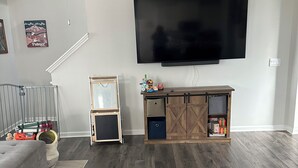 Een woonkamer met een flatscreen televisie, een plafondventilator, een houten kast en een grijze bank.