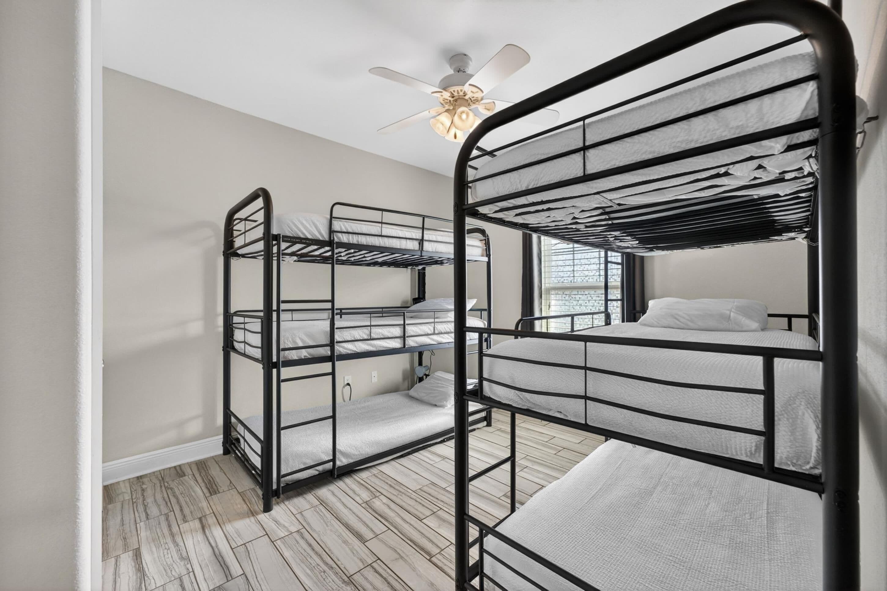 Une chambre avec des lits superposés, un ventilateur de plafond et une fenêtre laissant entrer la lumière naturelle.