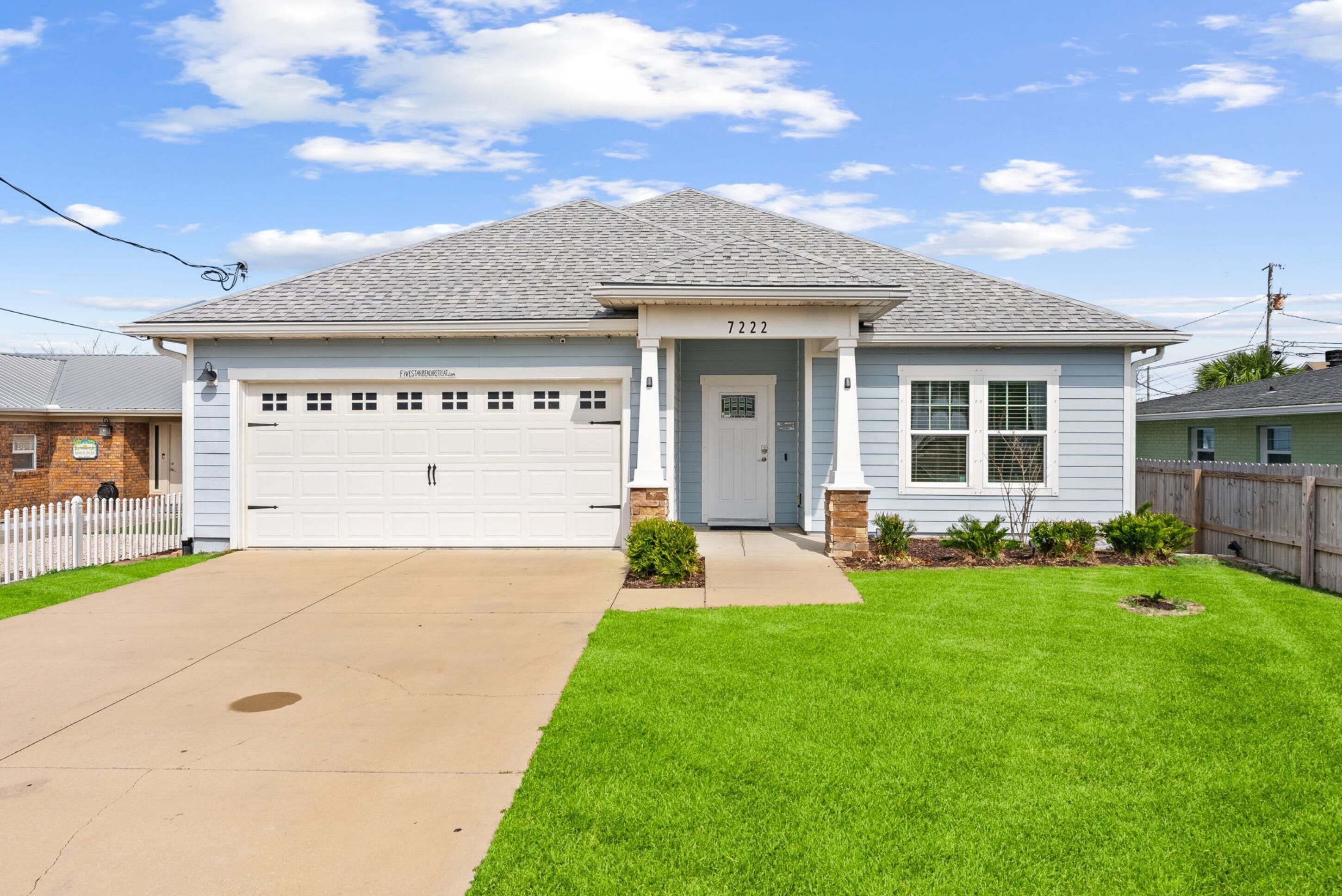 A single-story house with a garage, a front door, and a small front yard with grass and plants.