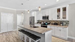 A modern kitchen with white cabinetry, granite countertops, stainless steel appliances, and a central island with bar stools. - Beach House - Tropic Like It's Hot (Panama City Beach)