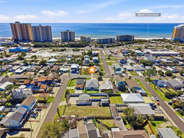 An aerial view of a residential area with beachfront access, featuring a mix of single-family homes and apartment buildings, a central road, and a prominent hotel with a beach view. - Beach House - Tropic Like It's Hot (Panama City Beach)
