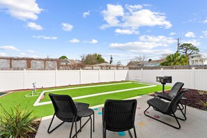 A backyard with artificial turf, two black wicker chairs, and a small table. - Beach House - Tropic Like It's Hot (Panama City Beach)