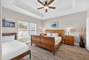 A bedroom with a wooden bed, two bedside tables, a ceiling fan, and a window with blinds. - Beach House - Tropic Like It's Hot (Panama City Beach)