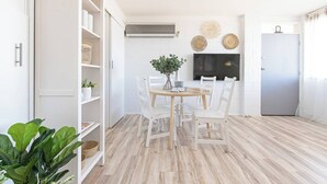 A modern kitchen with white cabinetry, a dining table with chairs, a TV mounted on the wall, and a refrigerator. - Scandi Beach Breeze Minutes from Glenelg Beach (Glenelg)