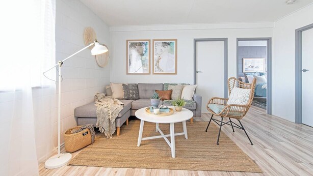 A modern living room with a grey sofa, a wicker chair, a round coffee table, and a floor lamp. There are two framed artworks on the wall and a basket on the floor. - Scandi Beach Breeze Minutes from Glenelg Beach (Glenelg)