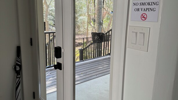 A hotel entrance with a sliding glass door, a 'No Smoking or Vaping' sign, a 'Before You Leave' notice, and a doormat. - Cozy 1-bedroom apartment in serene Rehoboth Beach with AC (Rehoboth Beach)