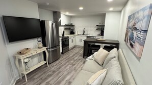 A modern living room with a striped sofa, a flat-screen TV, and a kitchen area with a refrigerator and stove. - Cozy 1-bedroom apartment in serene Rehoboth Beach with AC (Rehoboth Beach)