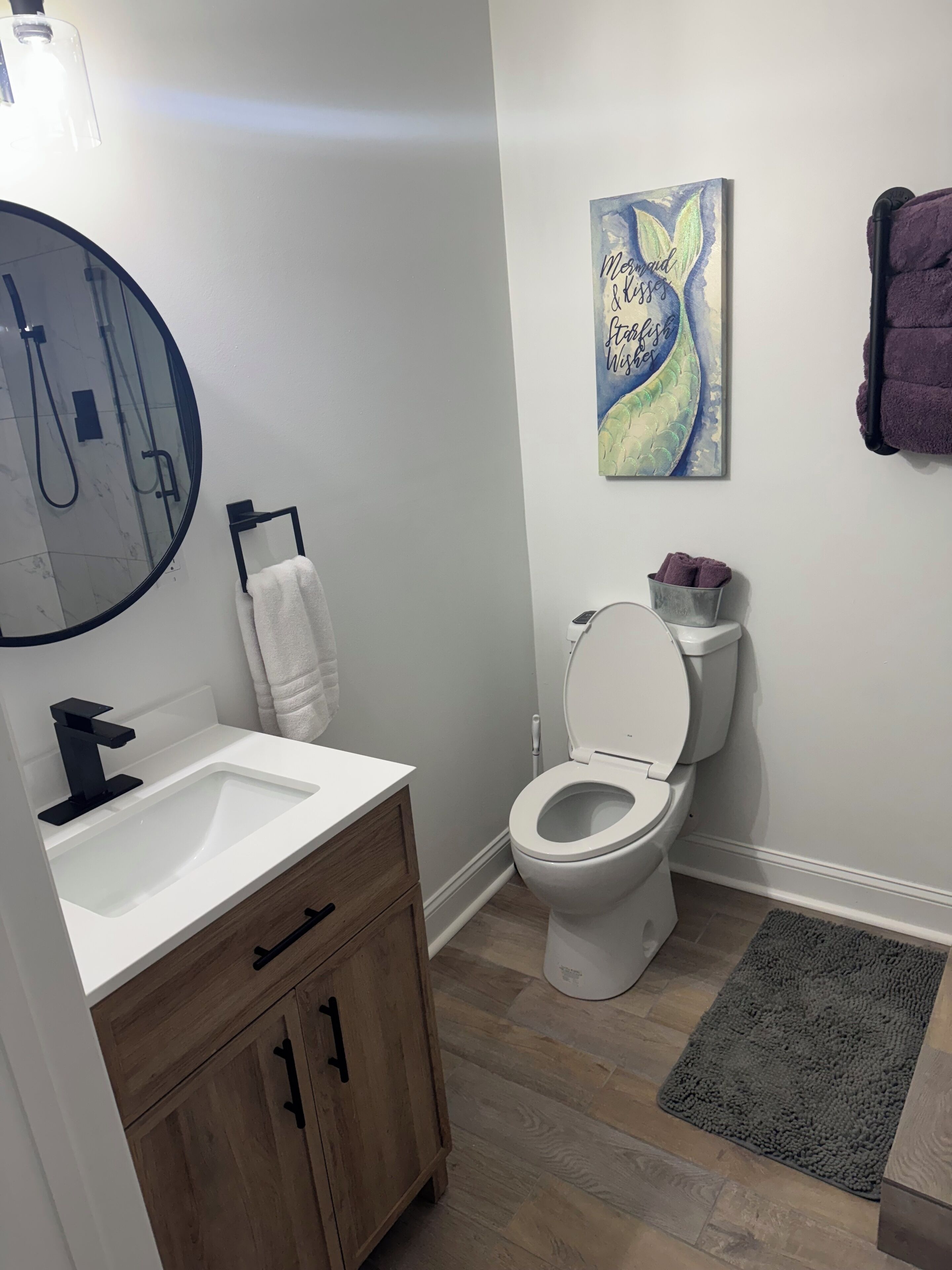 Un baño con lavamanos blanco, un mueble de madera, inodoro y toallero.