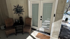 A covered patio area with two wicker chairs, a small table, and a decorative sun wall. There is a sliding glass door with a doormat. - Cozy 1-bedroom apartment in serene Rehoboth Beach with AC (Rehoboth Beach)