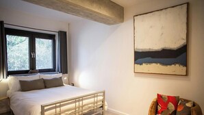 Un dormitorio con una cama, una silla, un cuadro y una ventana con persianas.