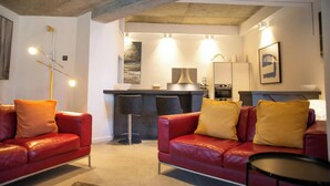 Una sala de estar moderna con sofás de cuero rojo, una mesa de centro negra y una zona de cocina al fondo.
