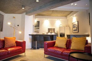 A modern living room with red leather sofas, a black coffee table, and a kitchen area in the background. - Y Bwncer, Tresaith - One Bedroom Cottage, Sleeps 2 (Tresaith)