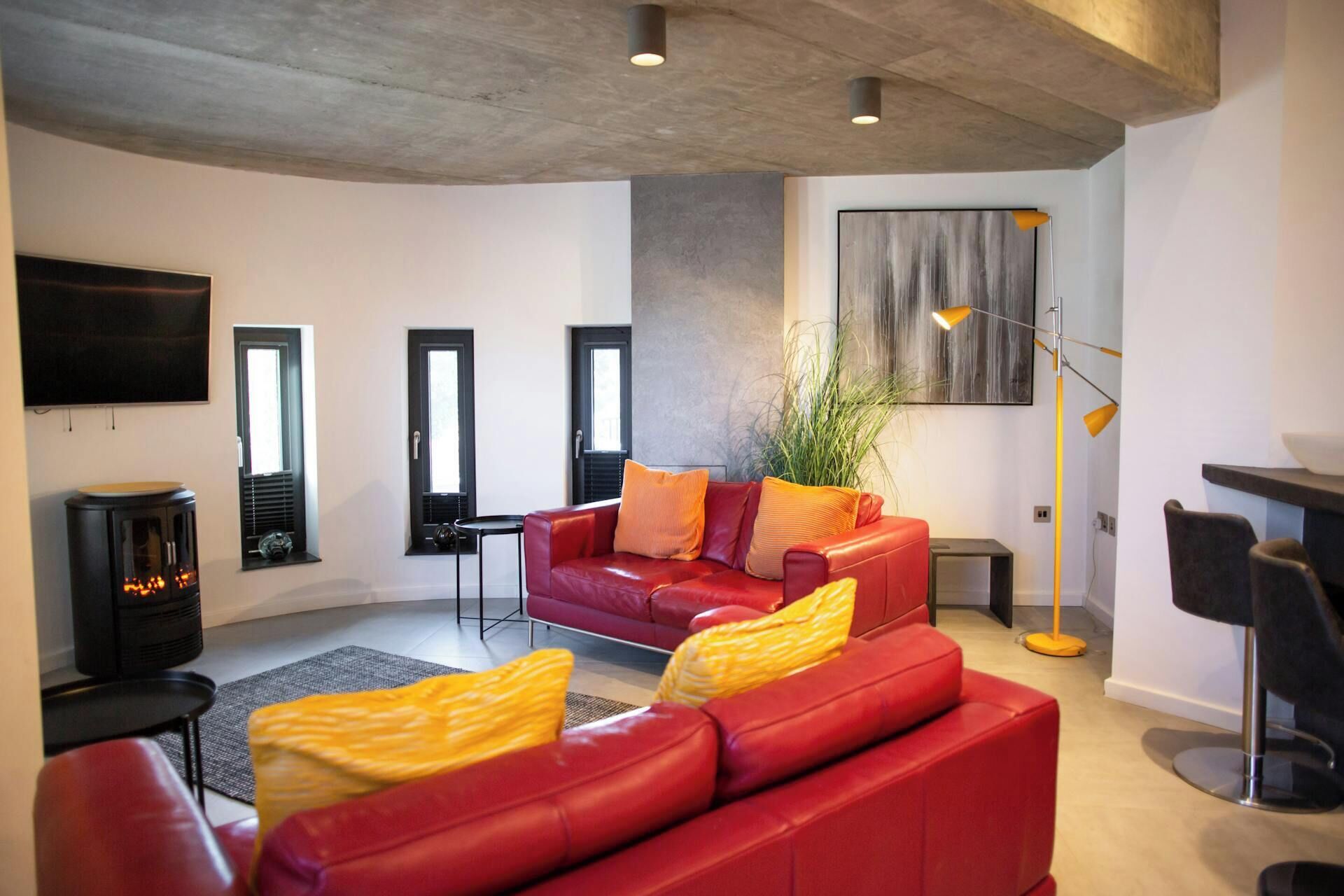 Un salon moderne avec un canapé en cuir rouge, un téléviseur noir et un lampadaire.