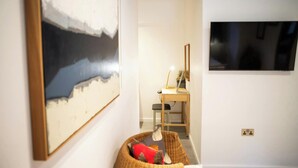 Una habitación con una obra de arte grande en la pared, un escritorio con una lámpara y un televisor fijado a la pared.