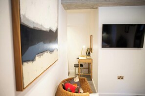 A room with a large framed artwork on the wall, a desk with a lamp, and a television mounted on the wall. - Y Bwncer, Tresaith - One Bedroom Cottage, Sleeps 2 (Tresaith)