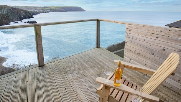 A wooden deck with a glass railing overlooking a coastal view. - Bay View, Tresaith - Two Bedroom Cottage, Sleeps 4 (Tresaith)