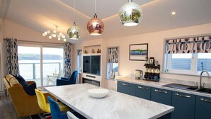 A modern kitchen with a central island, blue cabinets, and a view of the sea. - Bay View, Tresaith - Two Bedroom Cottage, Sleeps 4 (Tresaith)