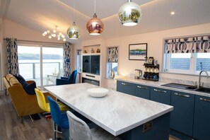 A modern kitchen with a central island, blue cabinets, and a view of the sea. - Bay View, Tresaith - Two Bedroom Cottage, Sleeps 4 (Tresaith)