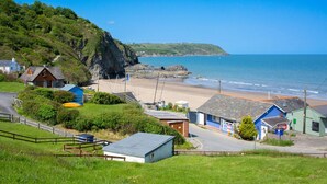 A coastal village with a sandy beach, a small harbor, and a prominent cliff. - Bay View, Tresaith - Two Bedroom Cottage, Sleeps 4 (Tresaith)