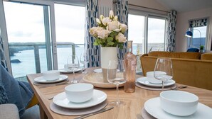A dining table set with white plates, bowls, and wine glasses, a vase with flowers, and a bottle of wine. - Bay View, Tresaith - Two Bedroom Cottage, Sleeps 4 (Tresaith)