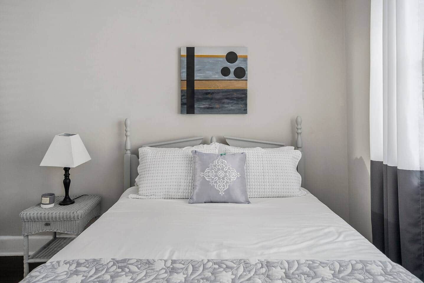 A neatly arranged hotel room with a bed, a bedside lamp, a small table, and a wall-mounted artwork.