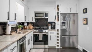 Une cuisine moderne avec des armoires blanches, un réfrigérateur en acier inoxydable, un four à micro-ondes, une cuisinière et un évier.