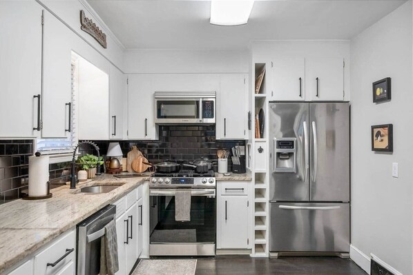 A modern kitchen with white cabinets, a stainless steel refrigerator, a microwave, a stove, and a sink.