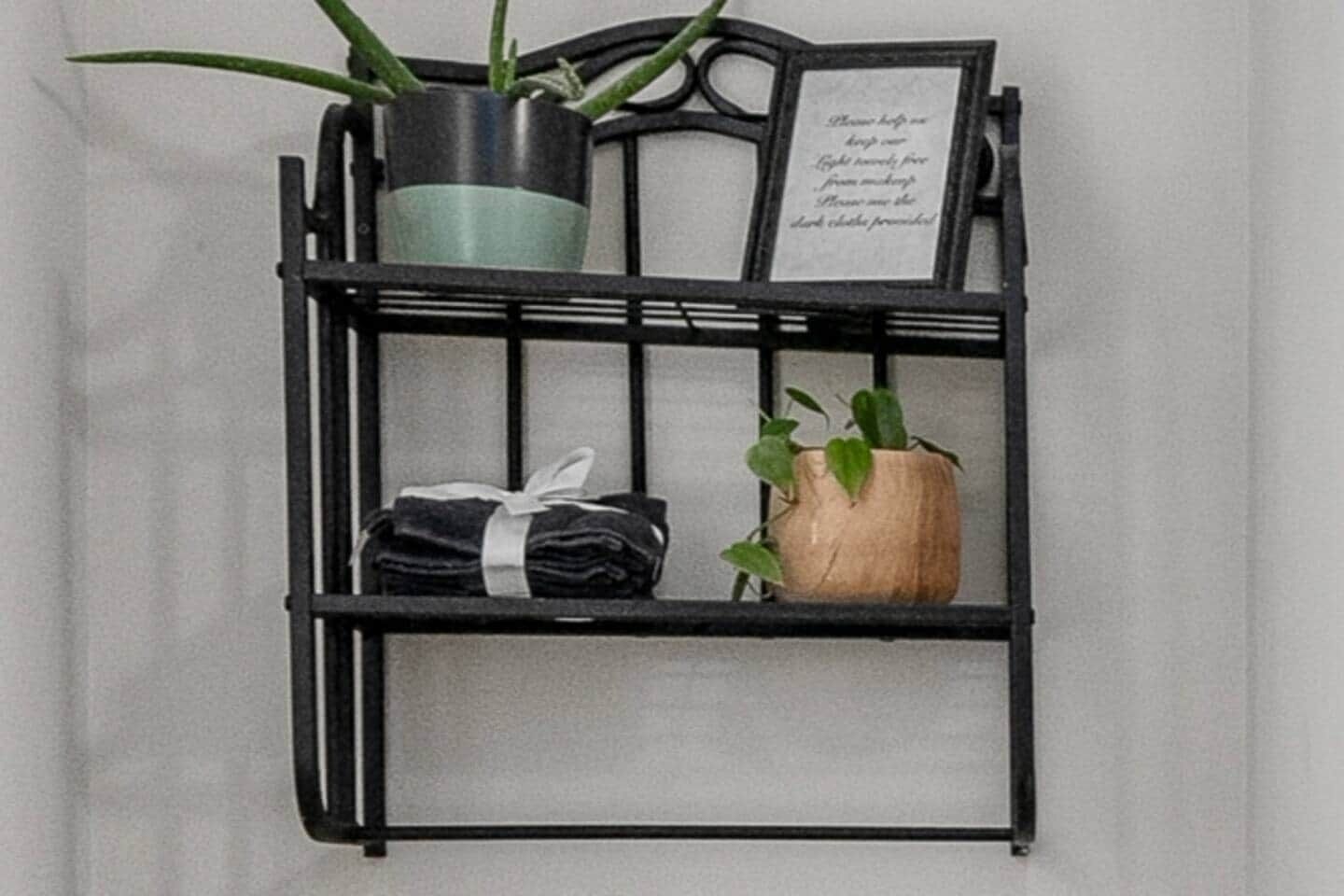 Una mensola in metallo nero con due piante in vaso e un biglietto incorniciato.
