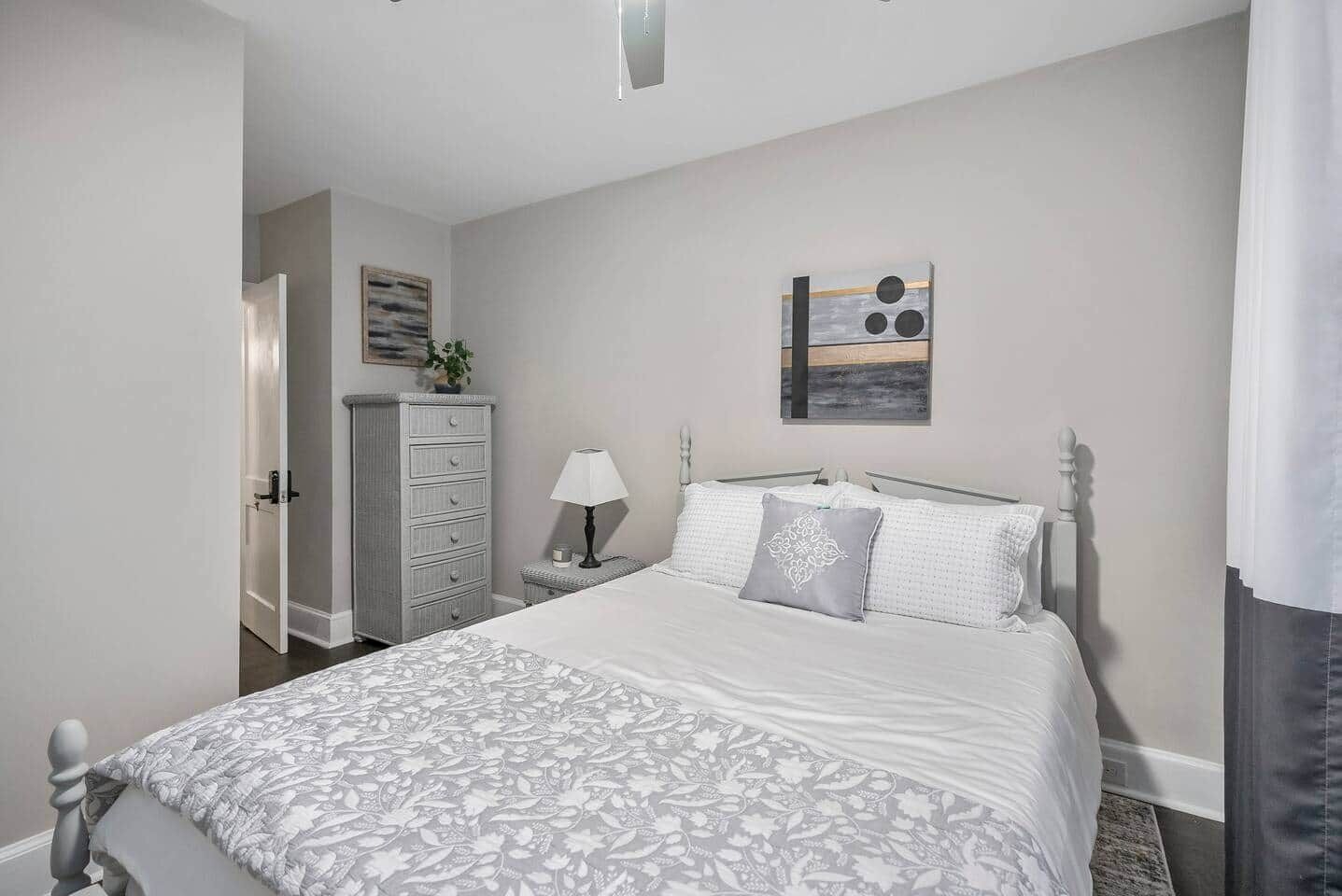 Een slaapkamer met een bed, een dressoir, nachtkastje, lamp en een kunstwerk aan de muur.