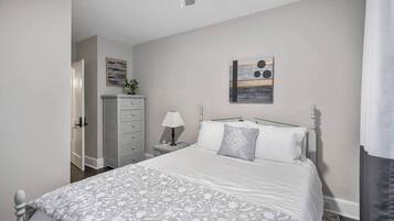 Een slaapkamer met een bed, een dressoir, nachtkastje, lamp en een kunstwerk aan de muur.