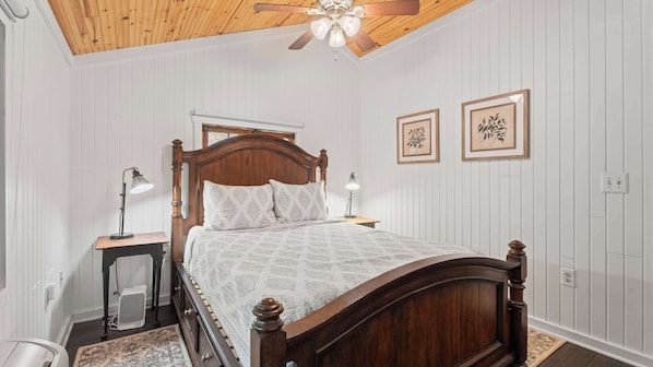 A bedroom with a wooden bed, two bedside lamps, a ceiling fan, and two framed pictures on the wall.