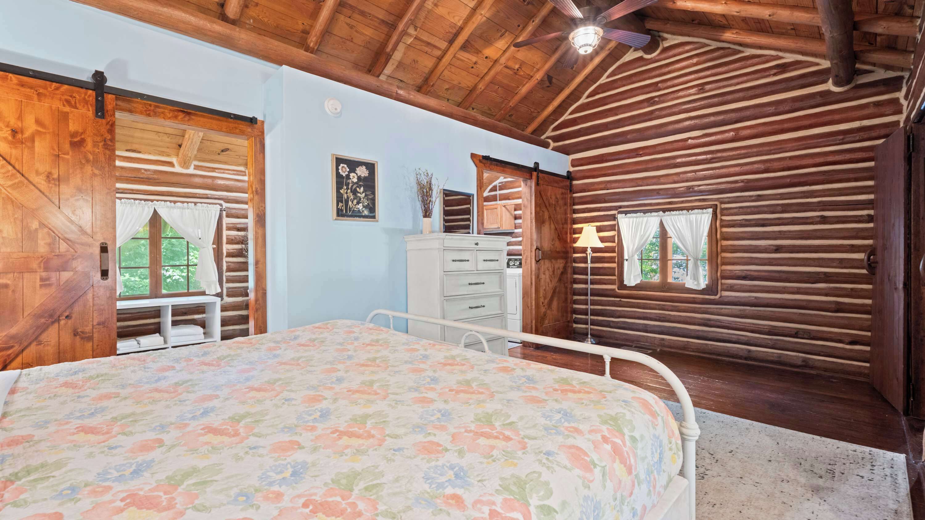 A log cabin bedroom with a bed, dresser, and a ceiling fan.