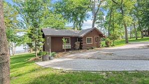 A wooden cabin with a sloped roof, a front porch, and a gravel driveway.