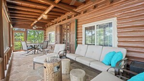 A log cabin with a stone patio, a sofa with pillows, and a dining table with chairs.